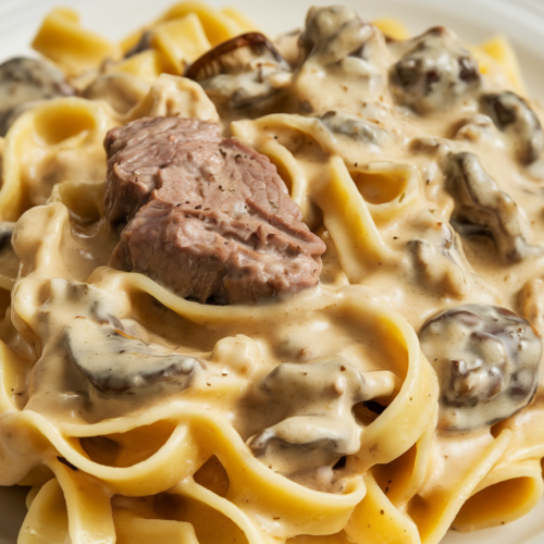 Close-up of tender beef stroganoff pasta noodles coated in silky cream sauce with mushroom pieces visible