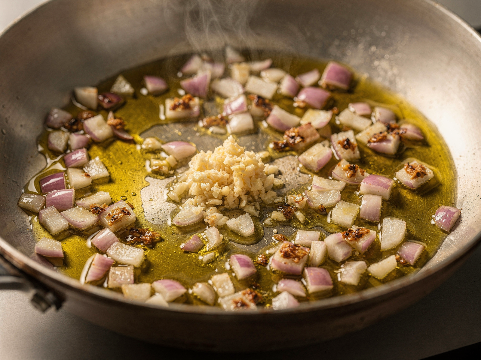 Close-up of diced red onion and minced garlic sautéing in olive oil in a large skillet, showing translucent onion pieces