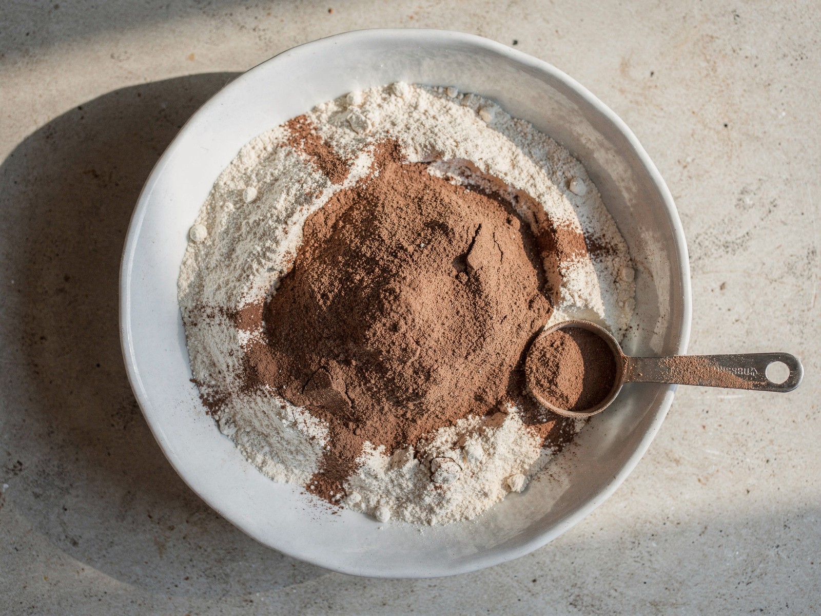 Dry ingredients for cocoa and chocolate pasta recipe mixed in a white bowl with cocoa powder visible